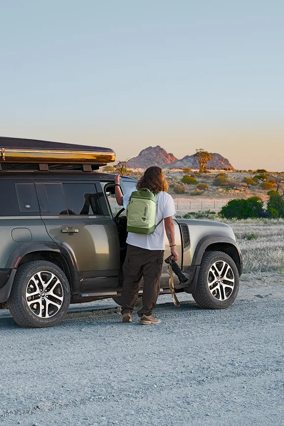Abenteurer mit Rucksack auf dem Weg zu einem Geländewagen mit Dachbox.